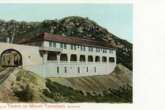 A vintage postcard shows the Tavern on Mount Tamalpais in California, a large white building with arched windows and a red roof, set against a backdrop of rocky hills. A railway track runs beside the structure.