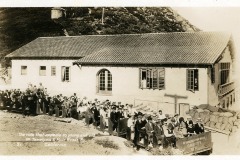 A large group of people are about descend the summit of Mt. Tamalpais, on the Gravity ride. The Mt. Tamlpais Tavern with tiled roof is seen in the background.