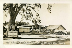 Vintage photo of Nut Tree in Vacaville, California, on Highway U.S. 40. The scene shows a rustic building surrounded by trees and a sign that reads Adventures in Good Eating. A classic car is parked in front of the establishment.