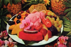 A colorful fruit platter with strawberries, grapes, pineapple, melon, and peaches surrounds scoops of pink ice cream topped with a flower. Pineapples and flowers decorate the background, adding a tropical vibe.