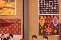 A group of people, including a family with children, sit around a table enjoying a meal in a retro dining setting. The walls are decorated with colorful, eclectic artwork featuring various patterns and designs.