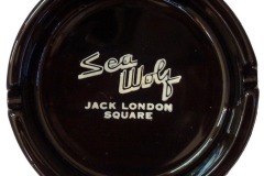 A round black ashtray features white  elegantly displaying Sea Wolf Restaurant above block letters stating Jack London Square.
